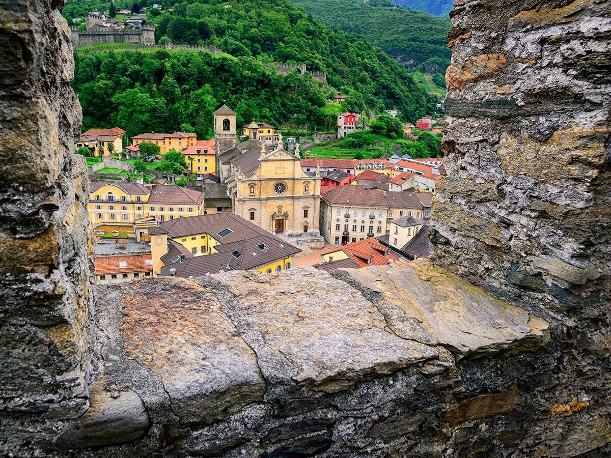 Panoramablick auf die Altstadt von Bellinzona, Schweiz, mit imposanter Kirche, bunten Häusern und grünen Bergen, durch ein Burgfenster.