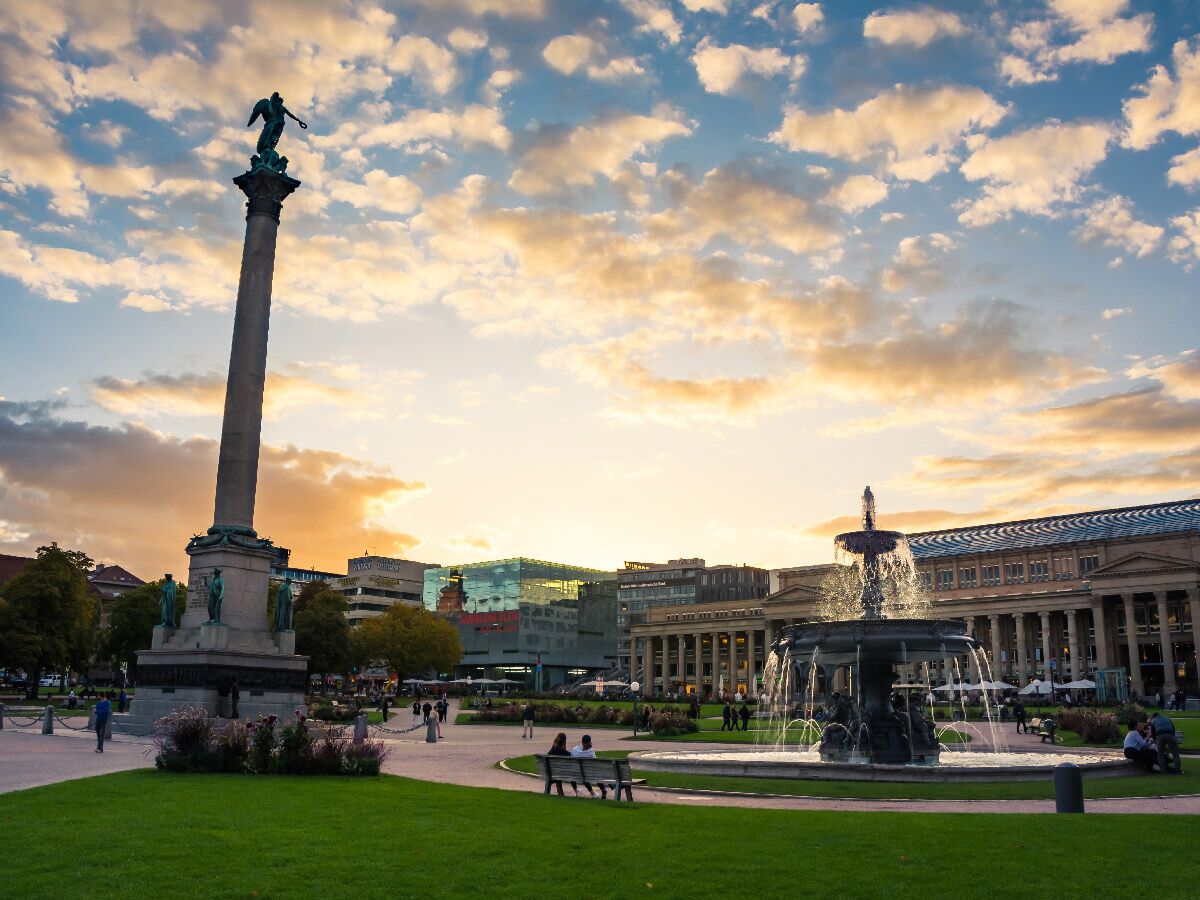 Panoramablick auf den Stuttgarter Schlossplatz bei Sonnenuntergang mit Jubiläumssäule, Brunnen und Neuem Schloss im Hintergrund.