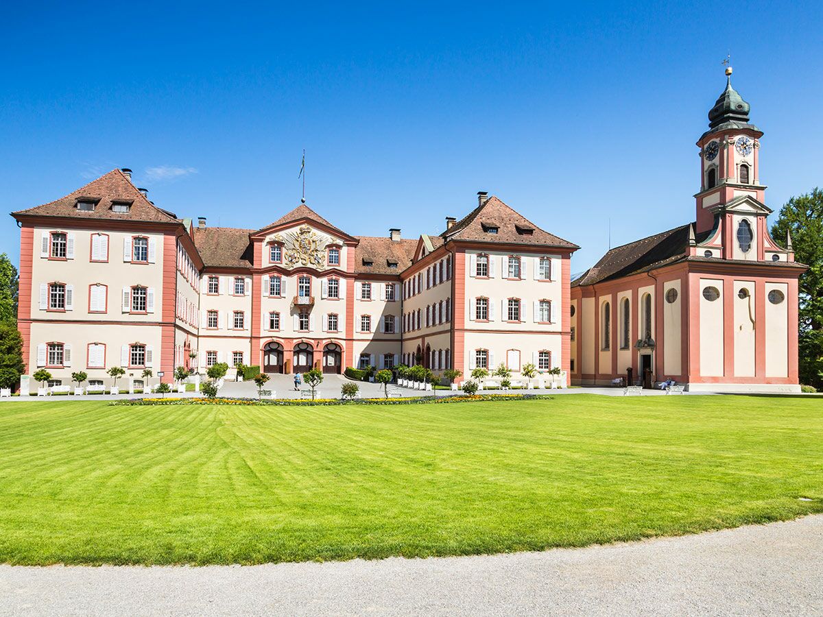 Barockes Schloss Salem mit markanter Kirche, weitläufigem grünen Rasen und blauem Himmel an einem sonnigen Tag.