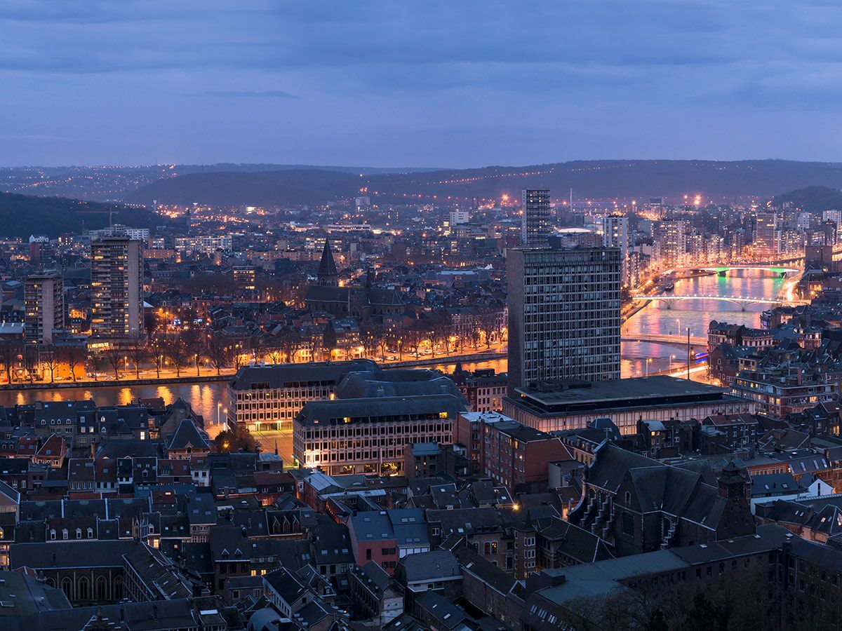 Panoramablick auf die beleuchtete Stadt Lüttich bei Nacht, mit Fluss Maas, Brücken und Hochhäusern.