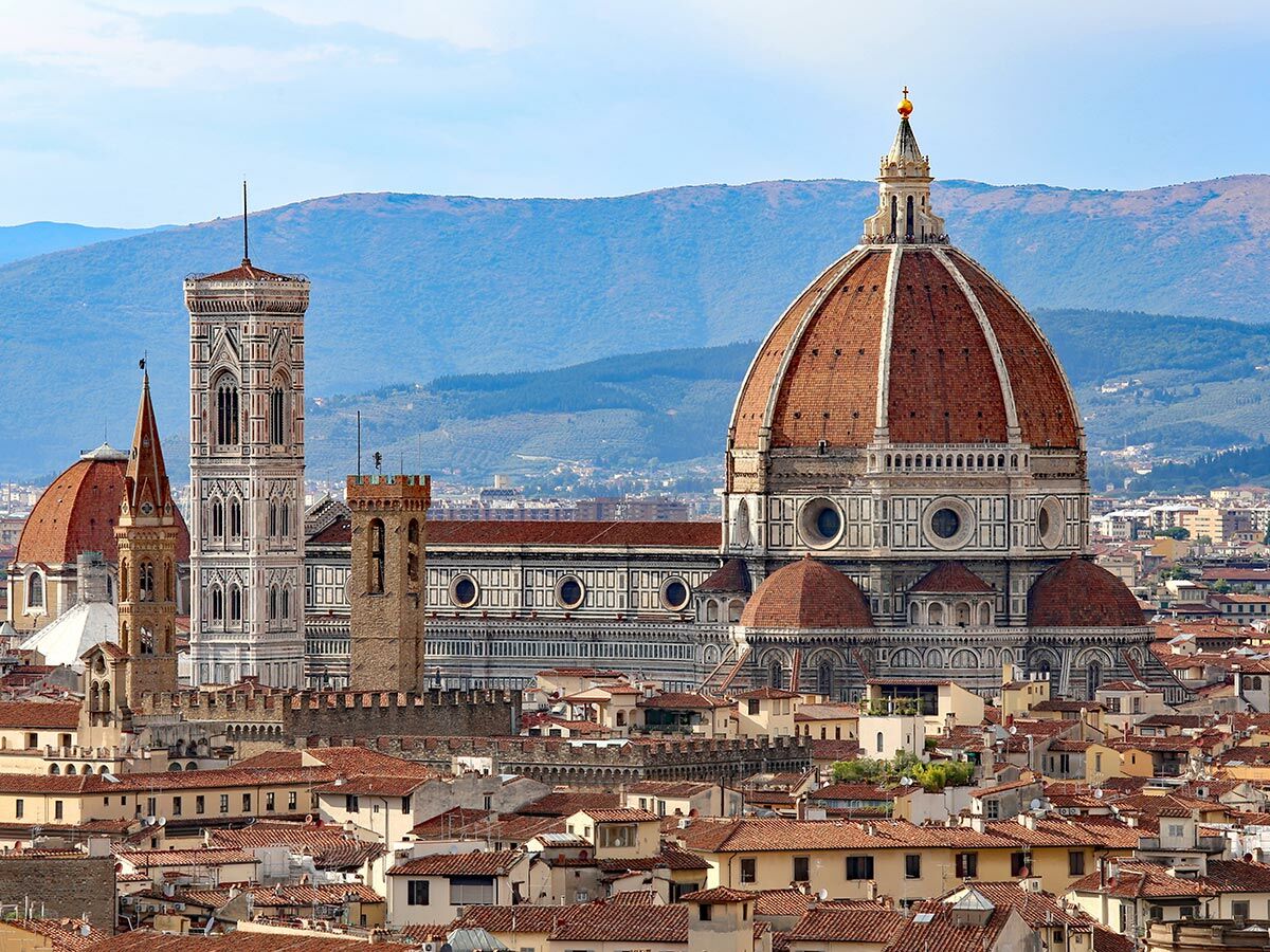 Panoramablick auf den Duomo und Giottos Campanile in Florenz, Italien, mit roten Dächern und Bergen.
