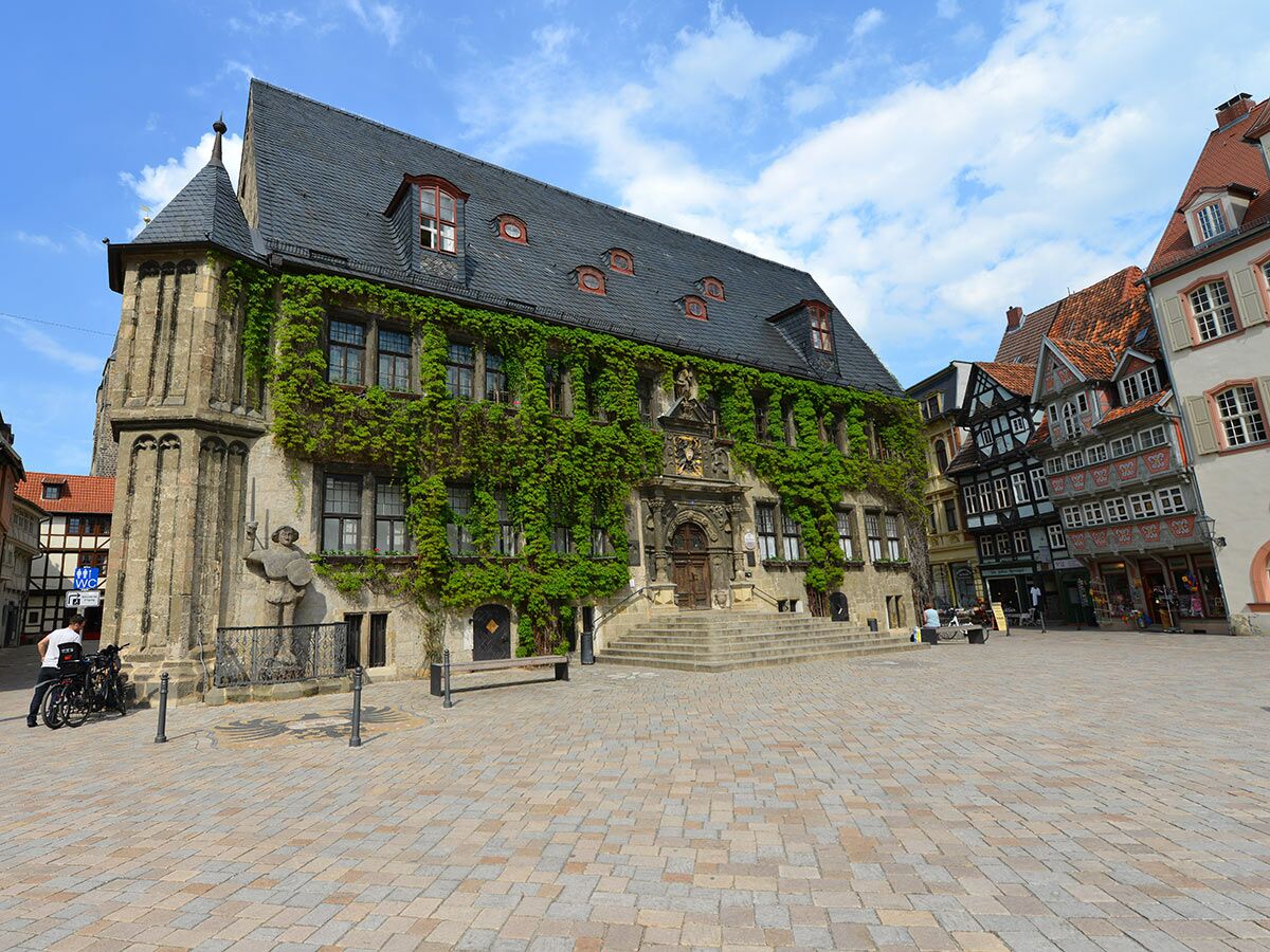 Altes Rathaus Göttingen mit Efeu, Rolandstatue, historischen Fachwerkhäusern am sonnigen Marktplatz unter blauem Himmel.