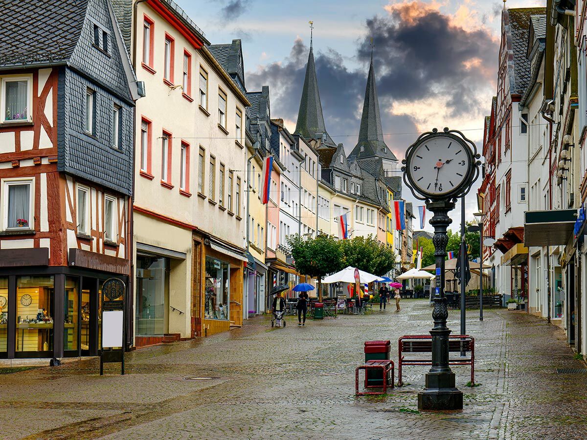 Malerische deutsche Altstadtstraße mit Kopfsteinpflaster, Fachwerkhäusern, Kirchtürmen und einer großen Uhr.