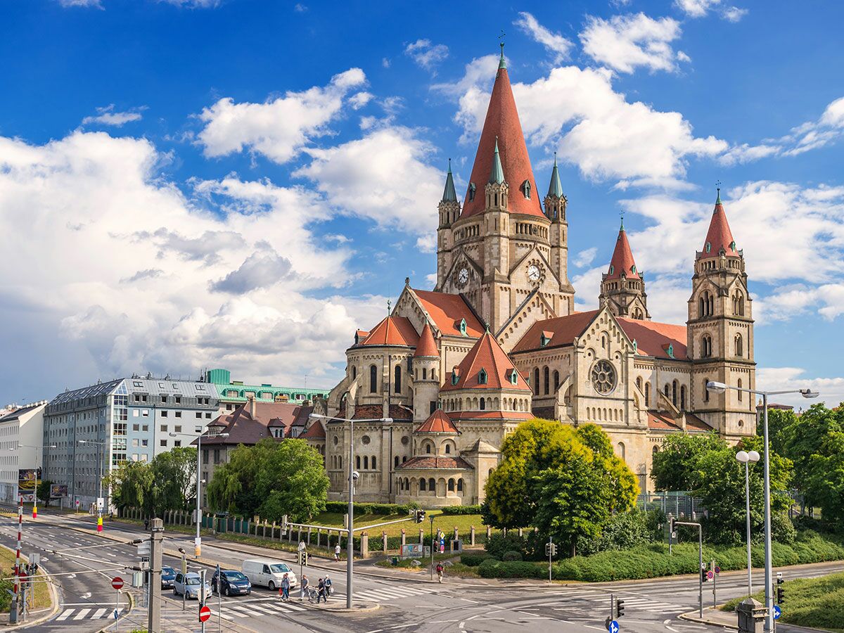 Die Franz-von-Assisi-Kirche (Mexikokirche) in Wien mit roten Dächern, blauer Himmel und einer belebten Kreuzung.