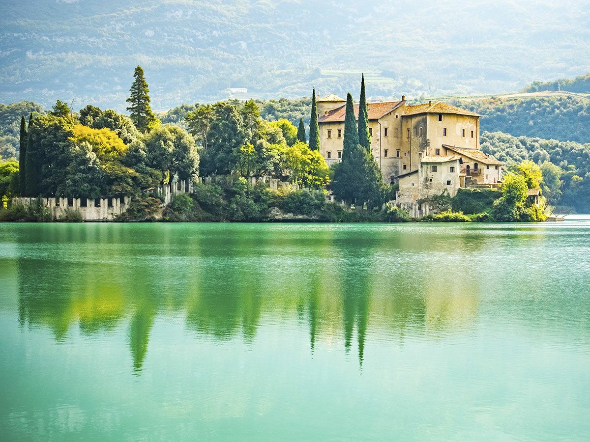 Castel Toblino, ein historisches Schloss am smaragdgrünen Tobliner See, umgeben von Bäumen und Bergen in den italienischen Alpen.