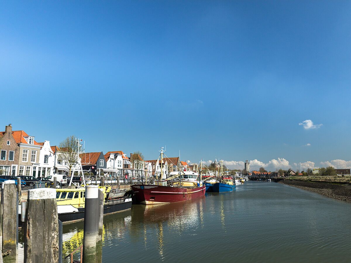 Malerische Hafenstadt mit bunten Fischerbooten an einer Gracht, gesäumt von traditionellen Häusern unter blauem Himmel.