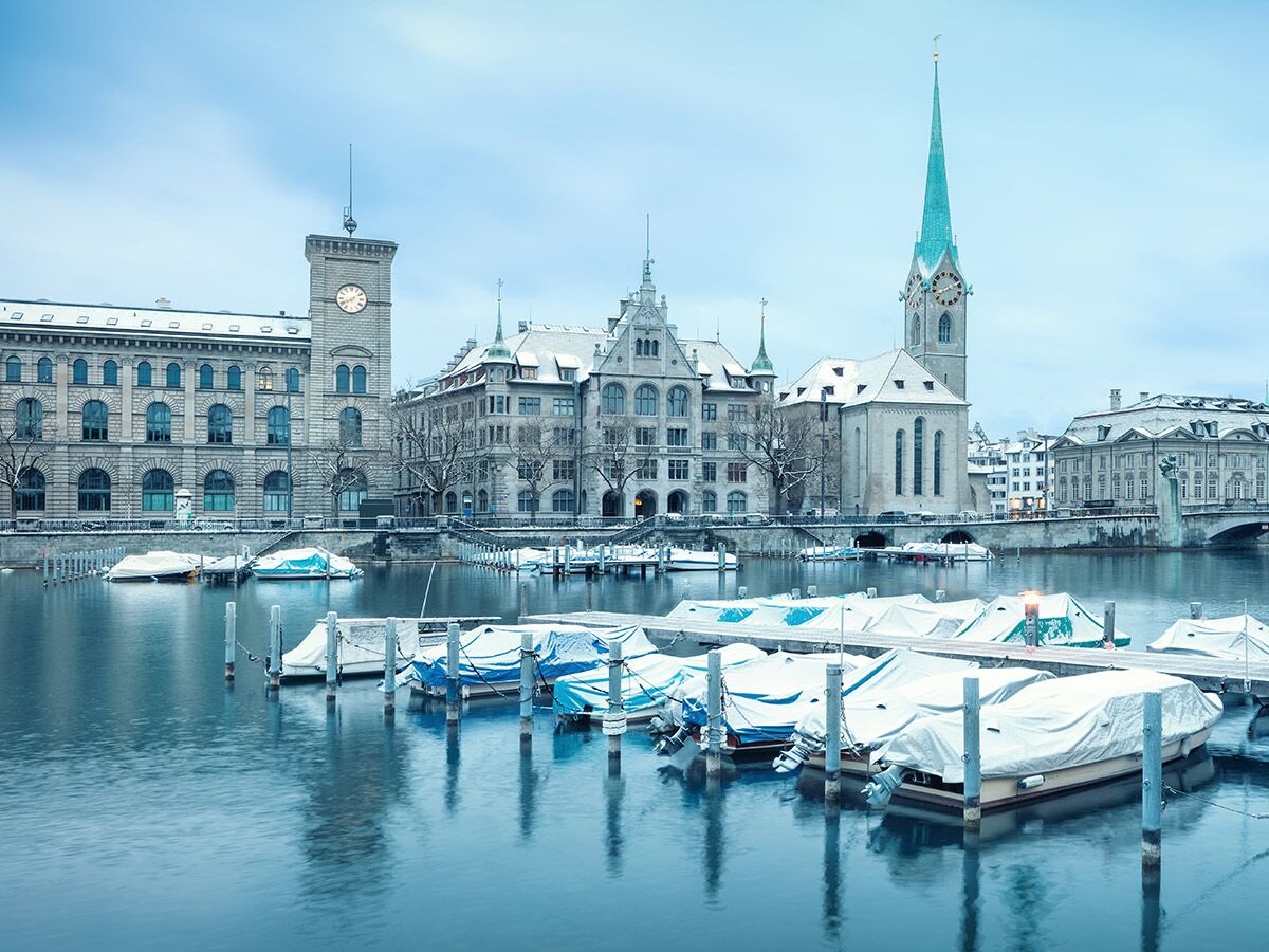 Winterlandschaft Zürich mit schneebedeckten Gebäuden, Fraumünster und St. Peter Kirche, und Booten auf dem Limmat Fluss.