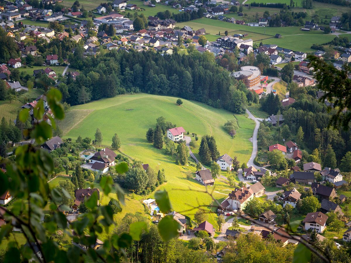 Luftaufnahme eines malerischen Dorfes in einem grünen Alpental mit vielen Häusern, Wäldern und sonnigen Wiesen.
