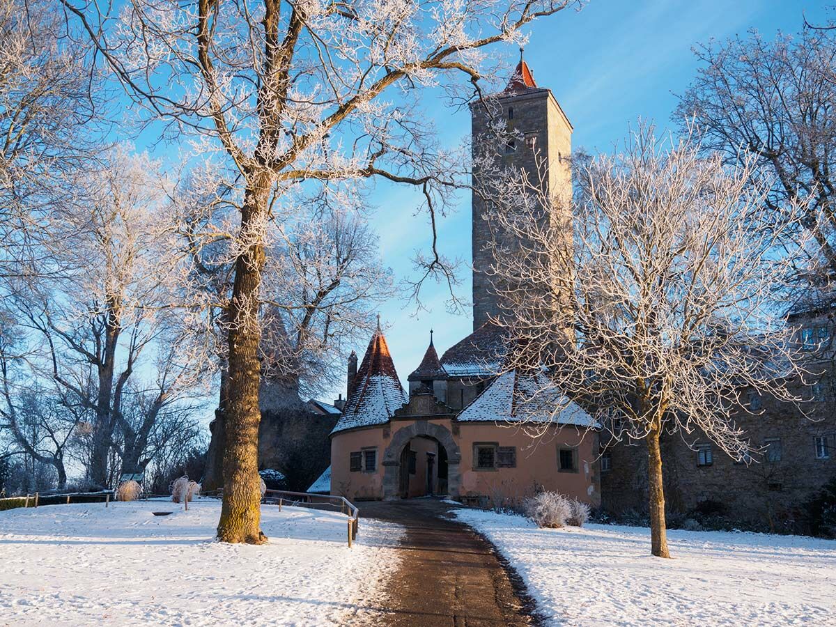 Historische Burg im Winter mit Reif auf Bäumen, Schnee und blauem Himmel. Ein Weg führt zum Torbogen.