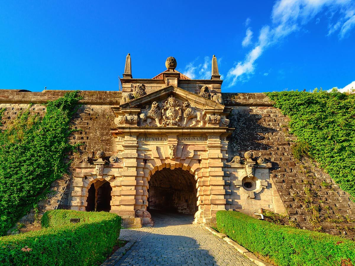Altes steinernes Burgtor einer Festung mit kunstvollen Verzierungen, grünem Efeu an der Mauer unter blauem Himmel.