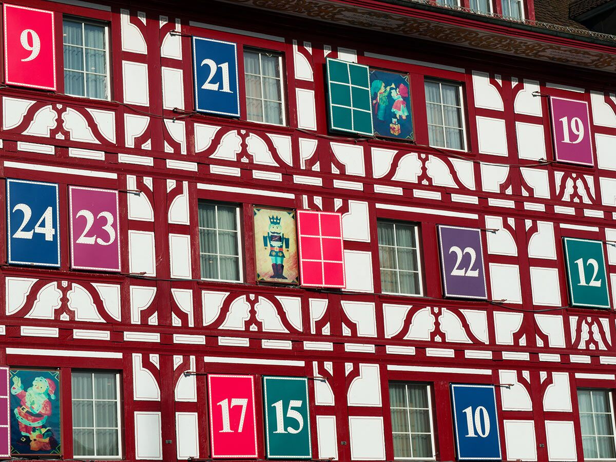 Rote Fachwerkfassade eines Gebäudes, das als riesiger Adventskalender mit bunten Fenstern und Weihnachtsbildern dient.