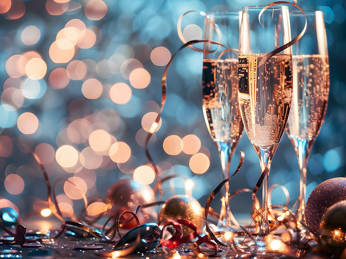 Drei Sektgläser mit Champagner, Konfetti, Bändern und goldenen Kugeln vor funkelnden Bokeh-Lichtern. Neujahrsfeier.