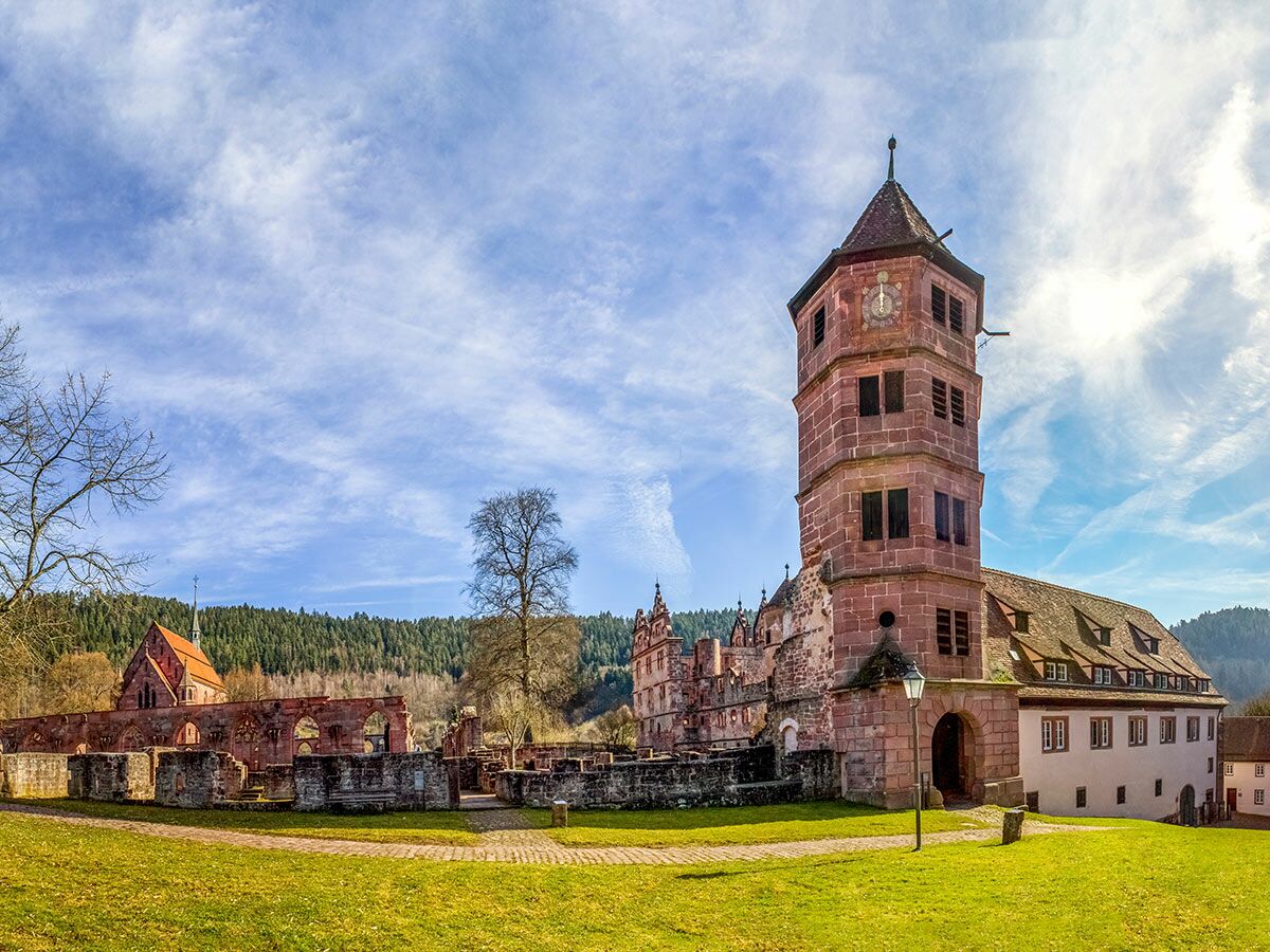 Historisches Kloster Hirsau im Schwarzwald mit markantem Uhrenturm, erhaltenen Gebäuden und Kirchenruinen unter blauem Himmel.