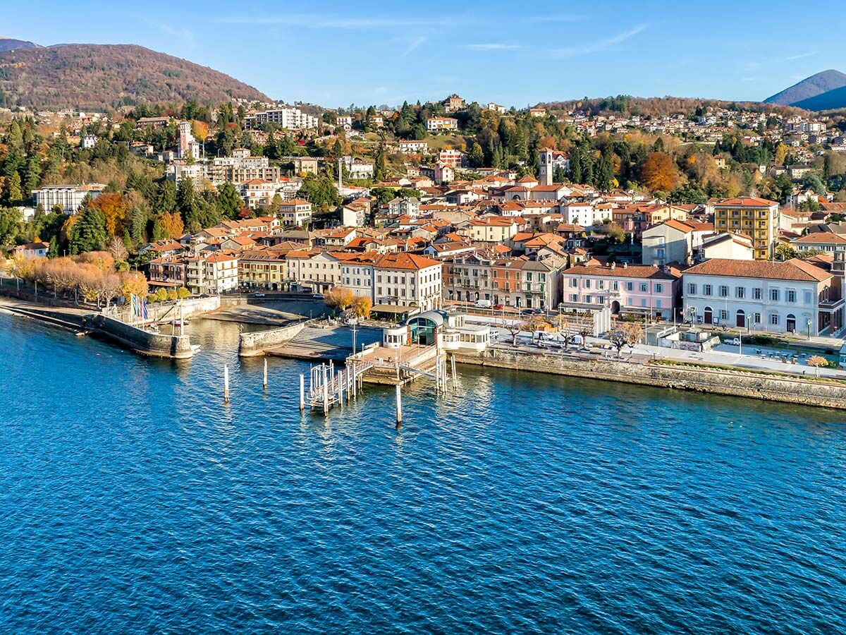Malerische Küstenstadt am blauen See mit farbigen Gebäuden, Bergen und Hafenanlagen unter strahlend blauem Himmel.