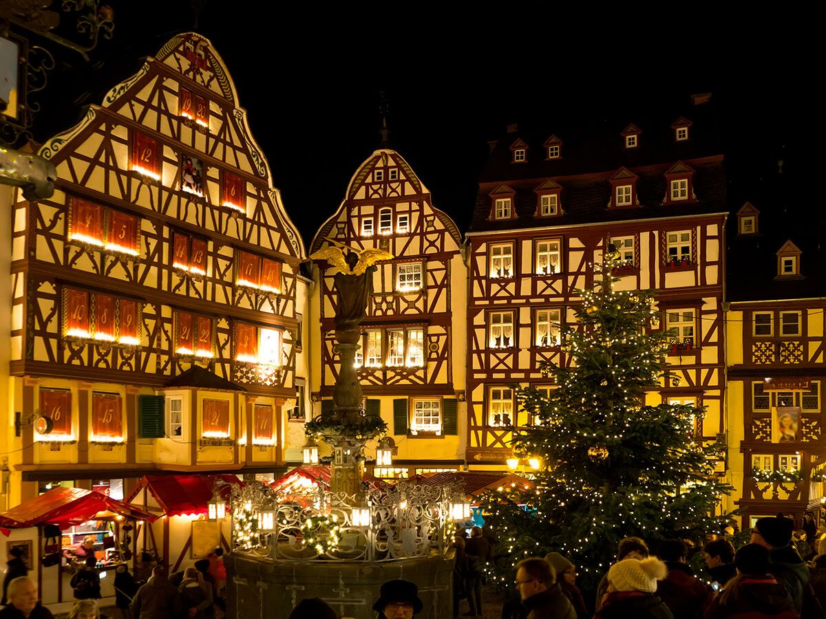 Festlicher Weihnachtsmarkt am Abend mit beleuchtetem Adventskalender-Fachwerkhaus, großem Weihnachtsbaum und Besuchern in Deutschland.