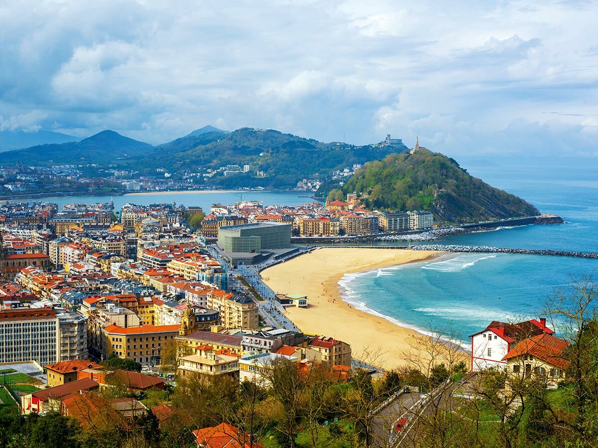 Panoramablick auf die spanische Küstenstadt San Sebastián mit La Concha Bucht, Strand, Stadtzentrum und Bergen im Hintergrund.