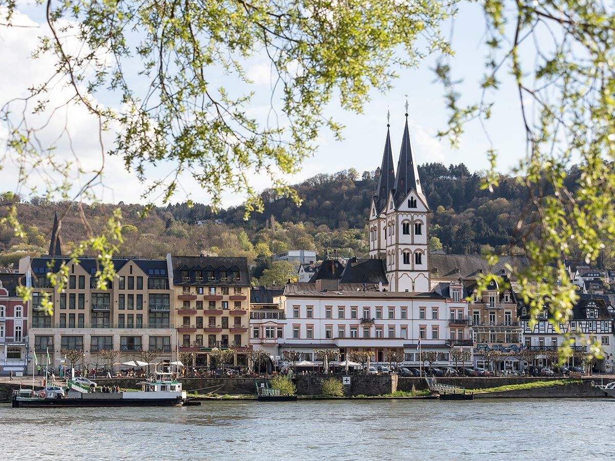 Historisches Bacharach am Rhein mit St. Peter Kirche, Fachwerkhäusern, Uferpromenade und Schiffsanleger im Sonnenschein.