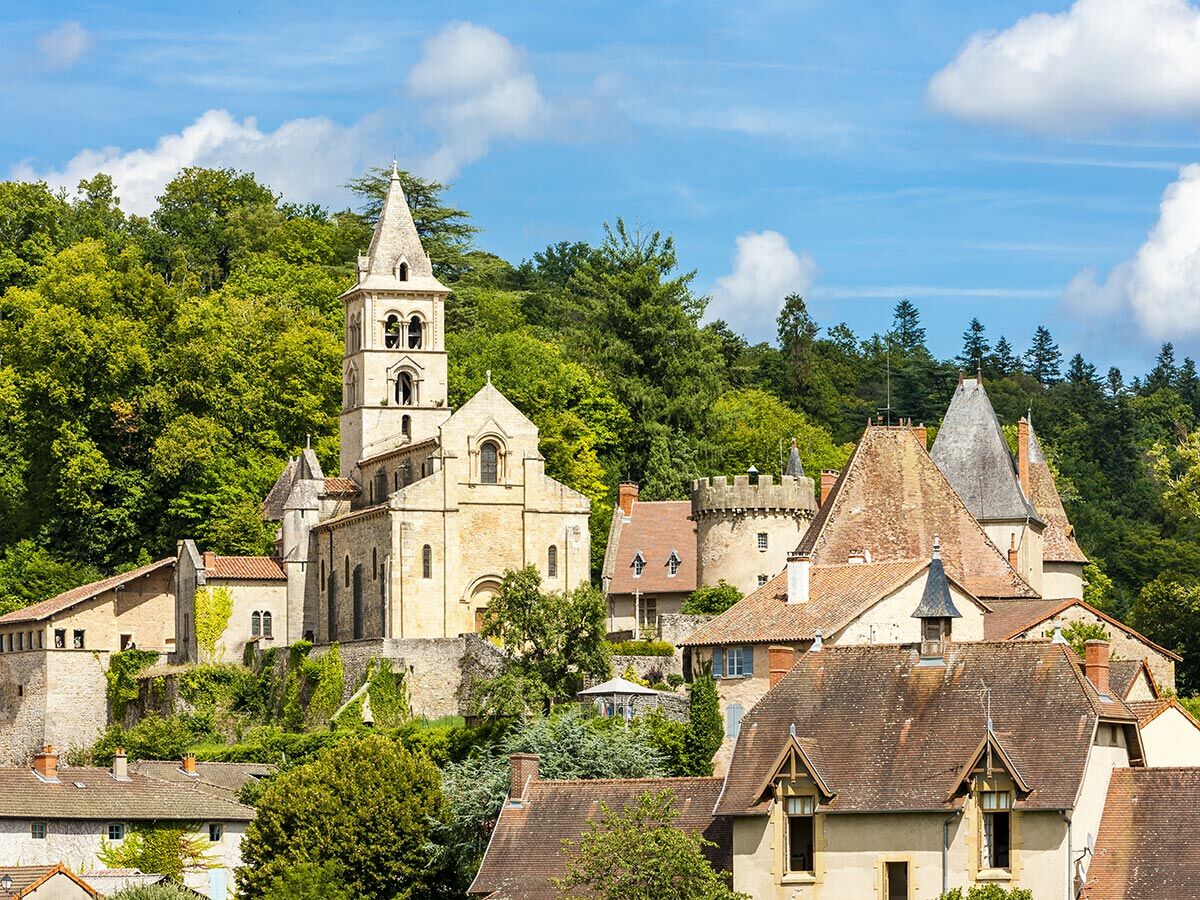 Historisches Dorf mit einer markanten Kirche und traditionellen Häusern, umgeben von dichtem Grün und Wald unter blauem Himmel.