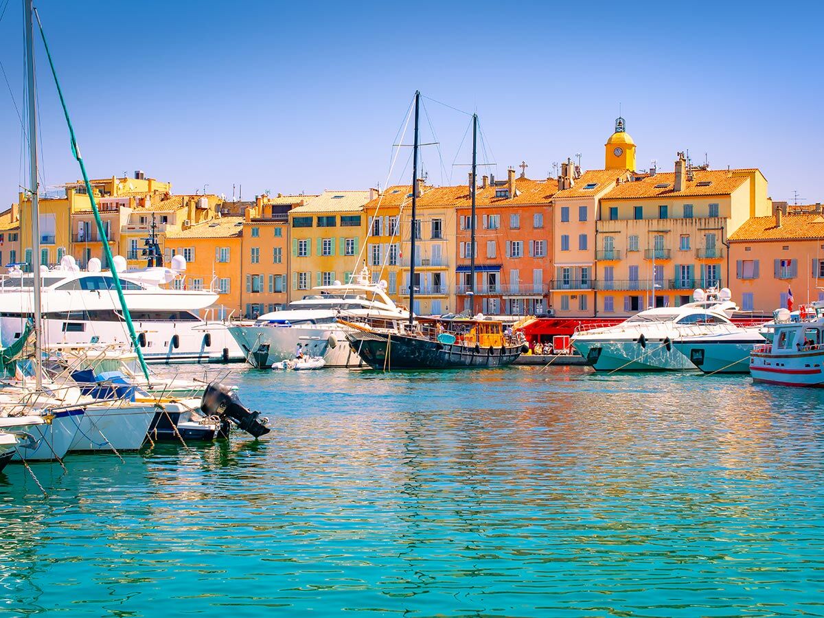 Blick auf den malerischen Hafen von Saint-Tropez mit bunten Gebäuden, Segelbooten und luxuriösen Yachten im türkisfarbenen Wasser.