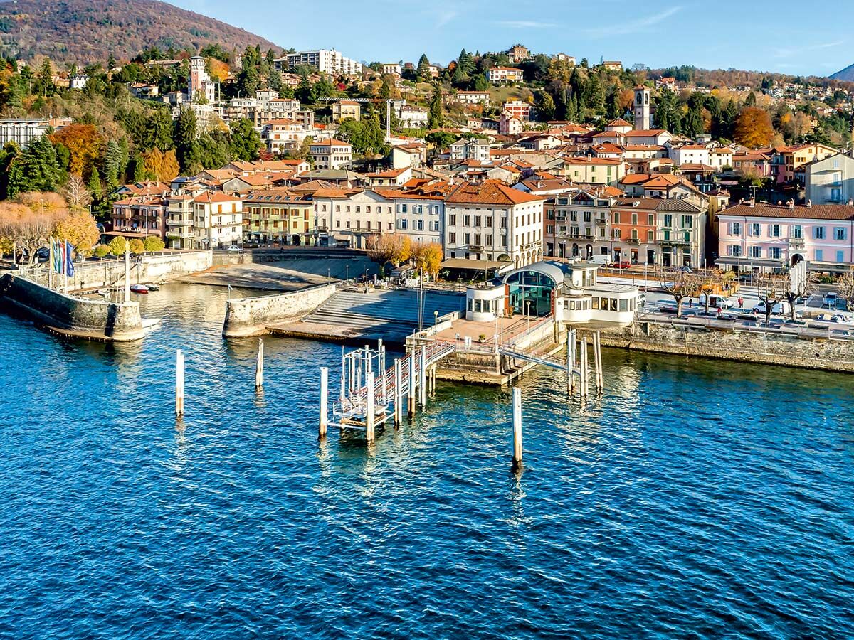 Panoramablick auf eine farbenfrohe italienische Seestadt mit Häusern am Hang, einem Pier und Booten im blauen Wasser.
