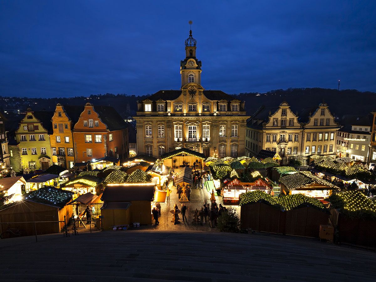 Festlicher Weihnachtsmarkt mit hell erleuchteten Ständen und historischem Rathaus in Tübingen bei blauer Abenddämmerung.