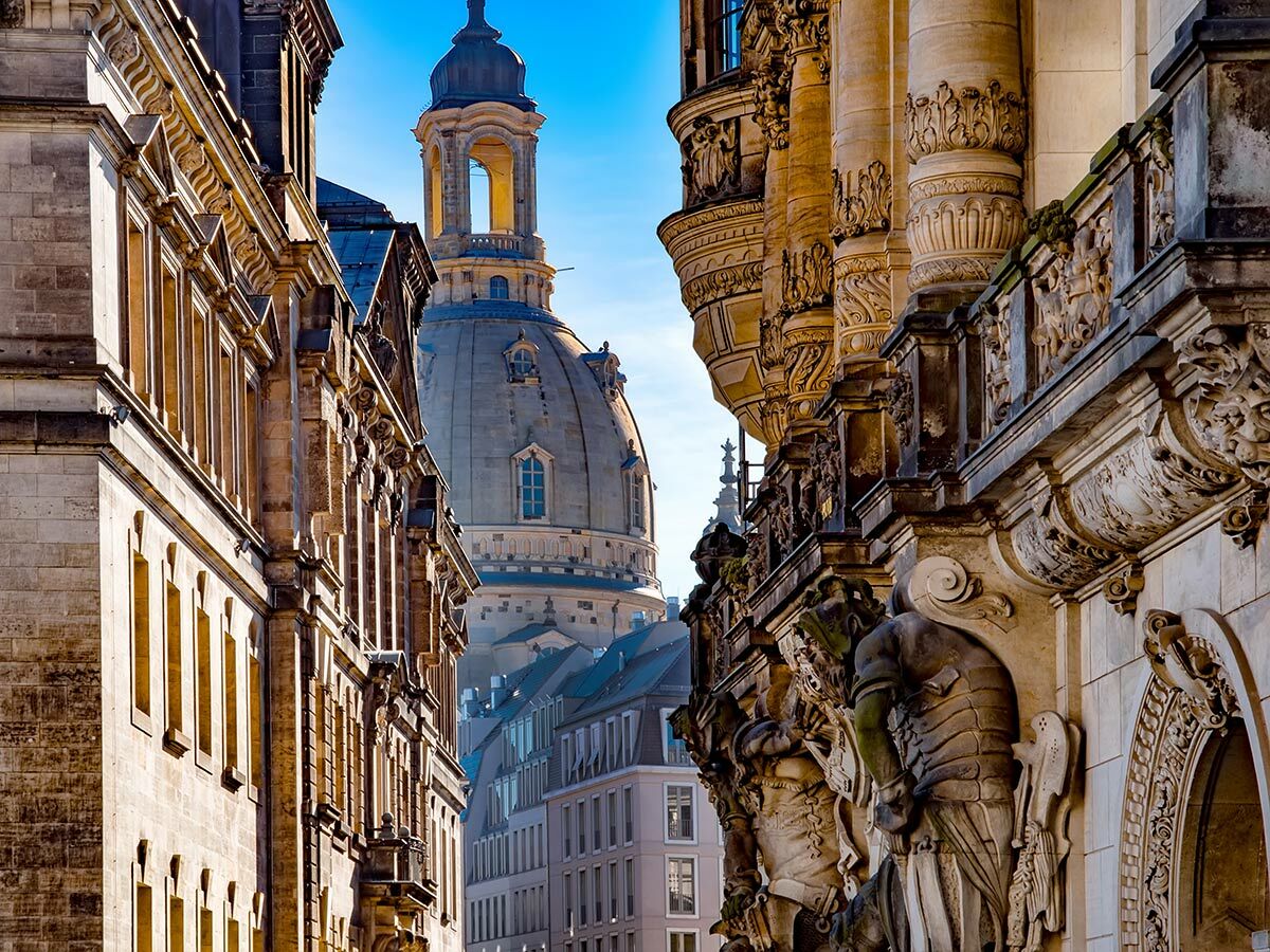 Blick auf die Frauenkirche in Dresden, umrahmt von historischen Gebäuden mit barocken Fassaden und Statuen.