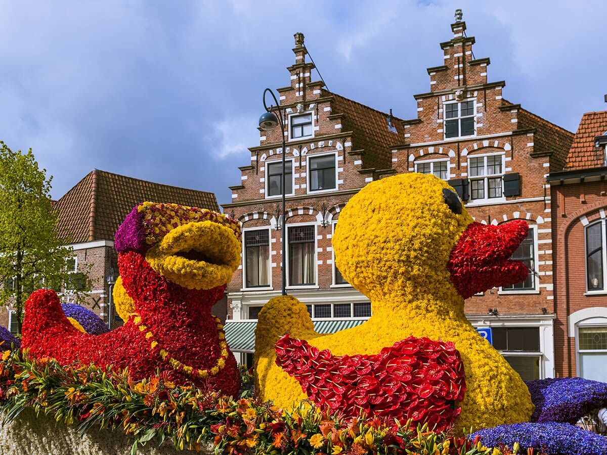 Zwei große, bunte Entenskulpturen aus Blumen bei einem Frühlingsfest in Holland vor traditionellen Giebelhäusern.