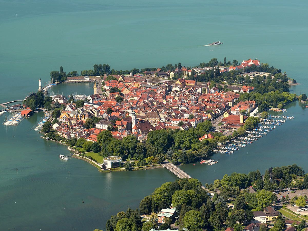 Luftaufnahme der Inselstadt Lindau im Bodensee mit Hafen, Leuchtturm, Booten und historischen Gebäuden unter blauem Himmel.