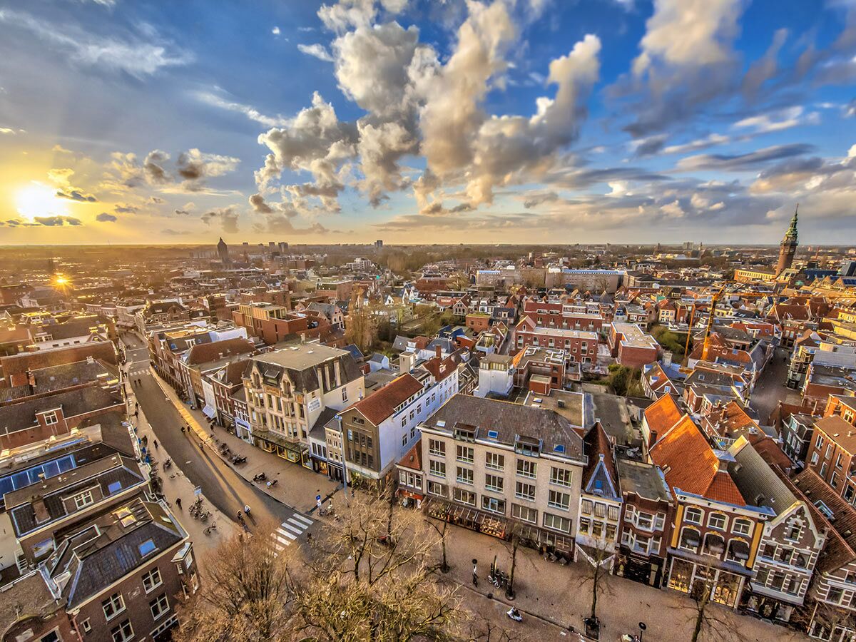 Luftaufnahme von Groningen bei Sonnenuntergang mit historischen Gebäuden, belebten Straßen und dem Martiniturm am Horizont.