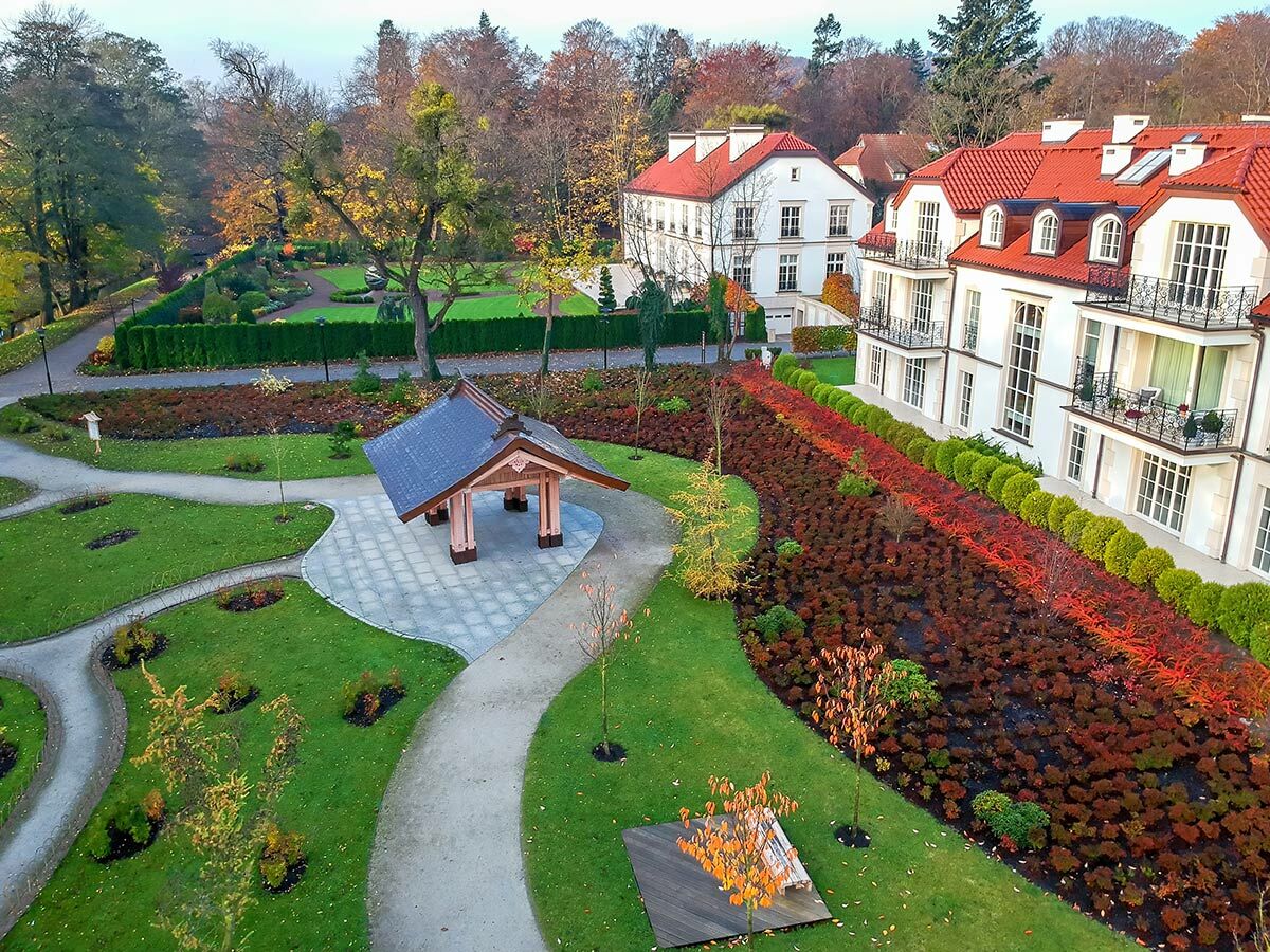 Luftaufnahme eines herbstlichen Parks mit modernen Villen, roten Dächern, einem japanischen Pavillon und bunten Sträuchern.