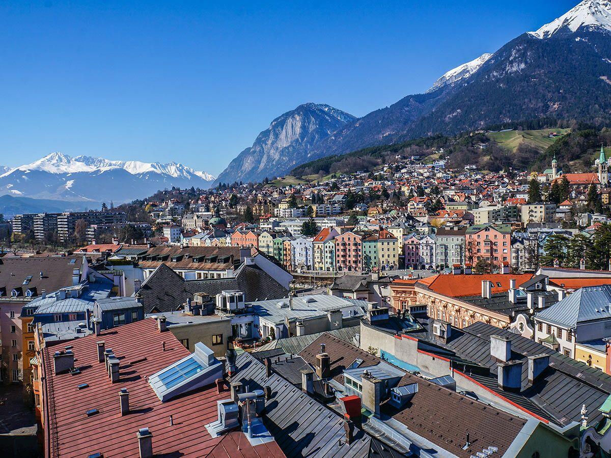 Panoramablick auf Innsbruck mit farbigen Häusern, Dächern und schneebedeckten Alpen im Hintergrund unter blauem Himmel.