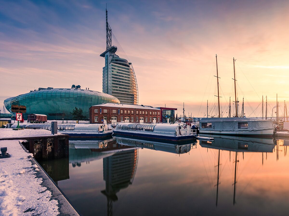 Winterlicher Hafen in Bremerhaven bei Sonnenuntergang mit moderner Architektur, Booten und Schnee, warmen Farben und Reflexionen.