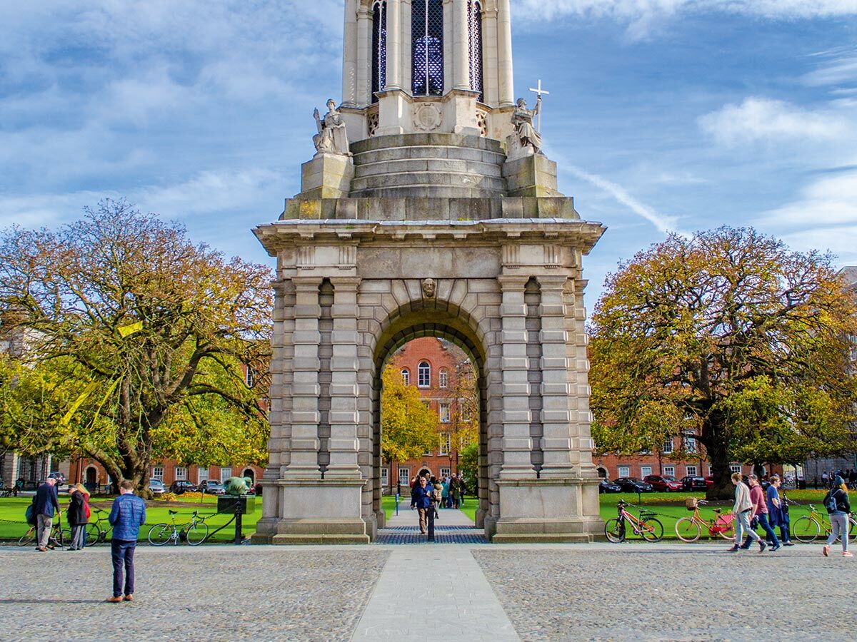 Campanile des Trinity College Dublin mit Studenten, Herbstbäumen und Rasenfläche an einem sonnigen Herbsttag in Irland.
