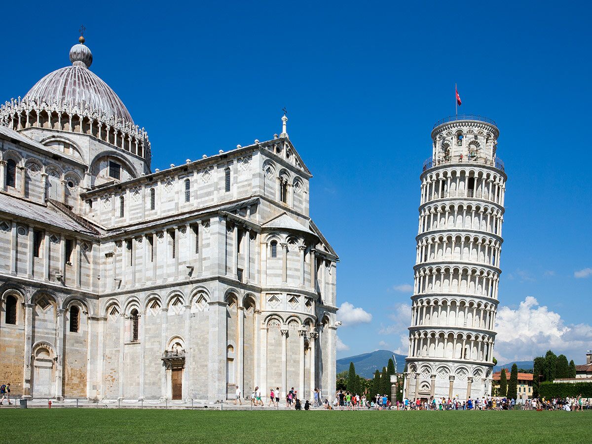 Der Schiefe Turm von Pisa und die Kathedrale von Pisa auf der grünen Piazza dei Miracoli unter blauem Himmel mit Touristen.