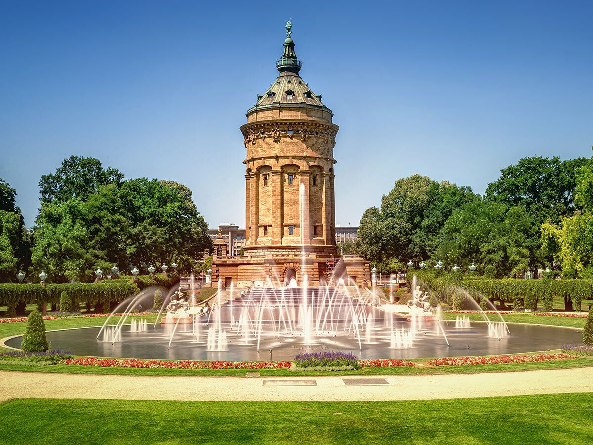 Der Wasserturm Mannheim mit seinen kunstvollen Brunnen und gepflegten Gärten unter blauem Himmel an einem sonnigen Tag.