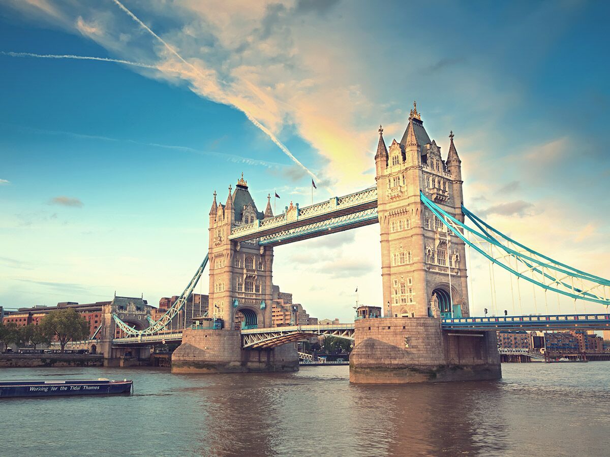Die ikonische Tower Bridge in London überspannt die Themse, mit warmem Licht des Sonnenaufgangs und einem Boot.