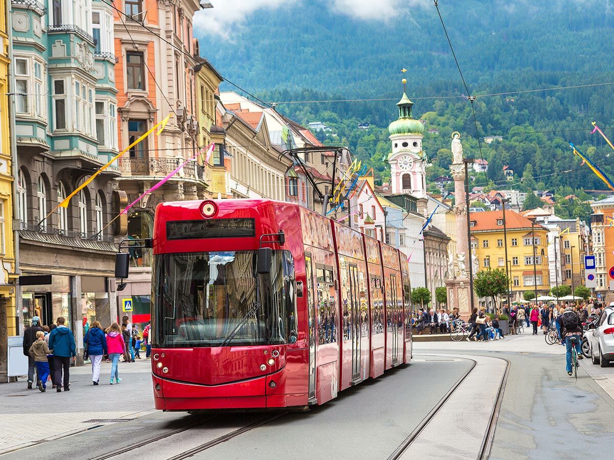 Moderne rote Straßenbahn fährt durch das historische Stadtzentrum von Innsbruck mit bunten Gebäuden und Bergen.