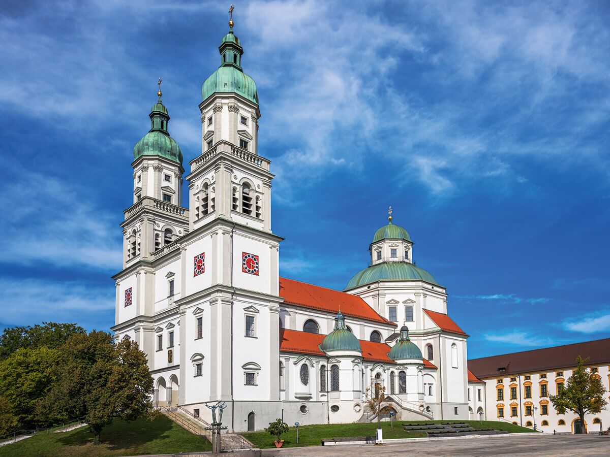 Kloster Andechs, eine prächtige weiße Barockkirche mit grünen Kuppeln und roten Dächern unter blauem Himmel in Bayern.