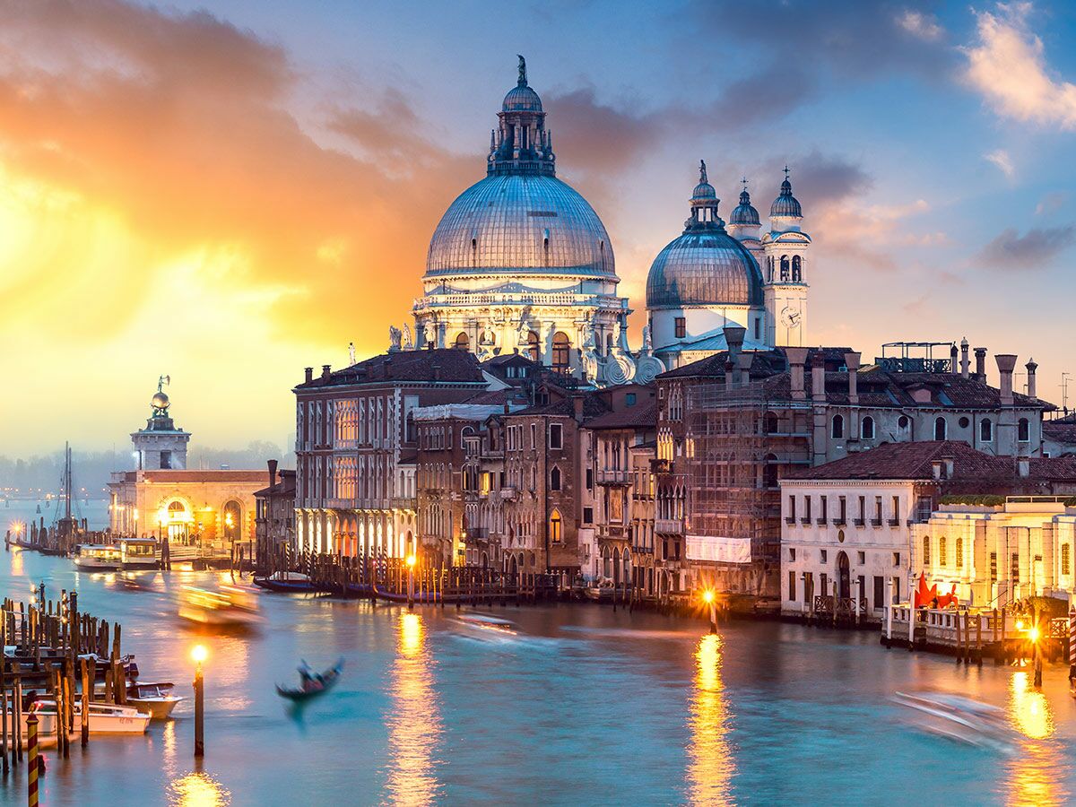Venedig bei Sonnenuntergang über dem Grand Canal mit Santa Maria della Salute, beleuchteten Gebäuden und Booten.