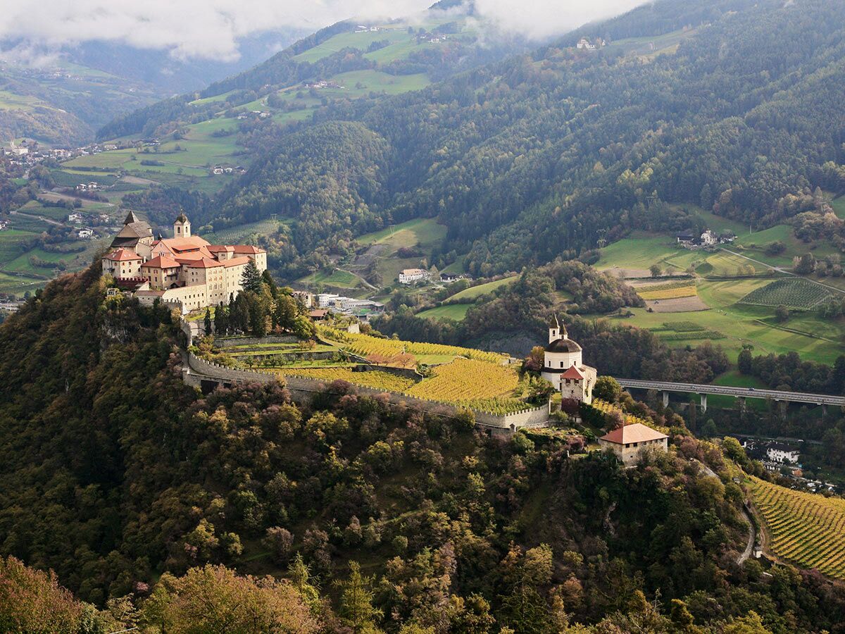 Das majestätische Kloster Neustift in Vahrn, Südtirol, thront auf einem Hügel, umgeben von goldenen Herbst-Weinbergen und Bergen.