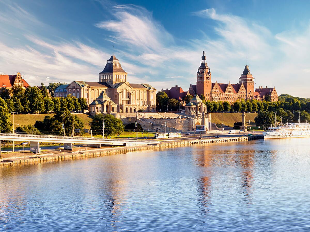 Panorama der Wały Chrobrego in Szczecin mit historischen Gebäuden, Fluss Oder, Brücke und Schiff bei Sonnenlicht.