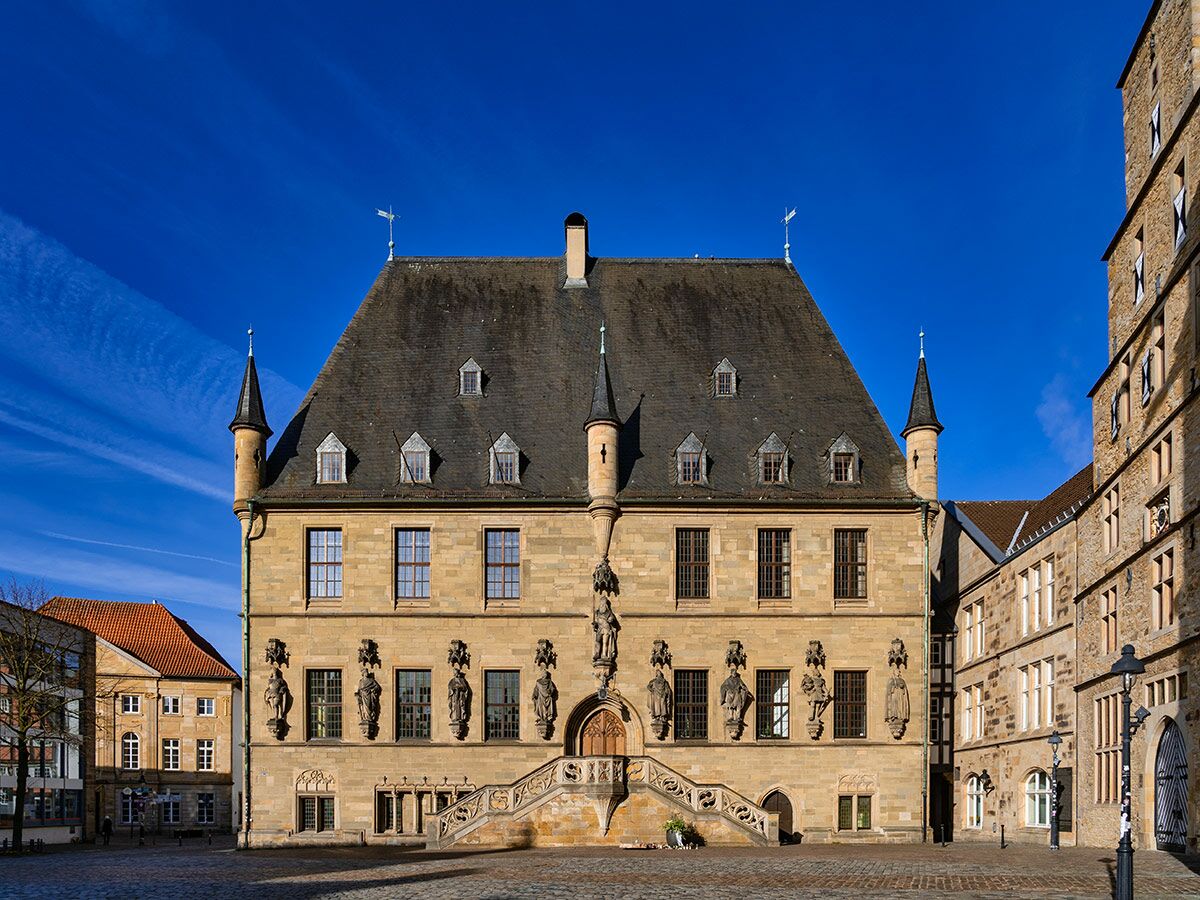Historisches Rathaus Paderborn mit Skulpturen, Treppe und Türmen unter blauem Himmel am Marktplatz.