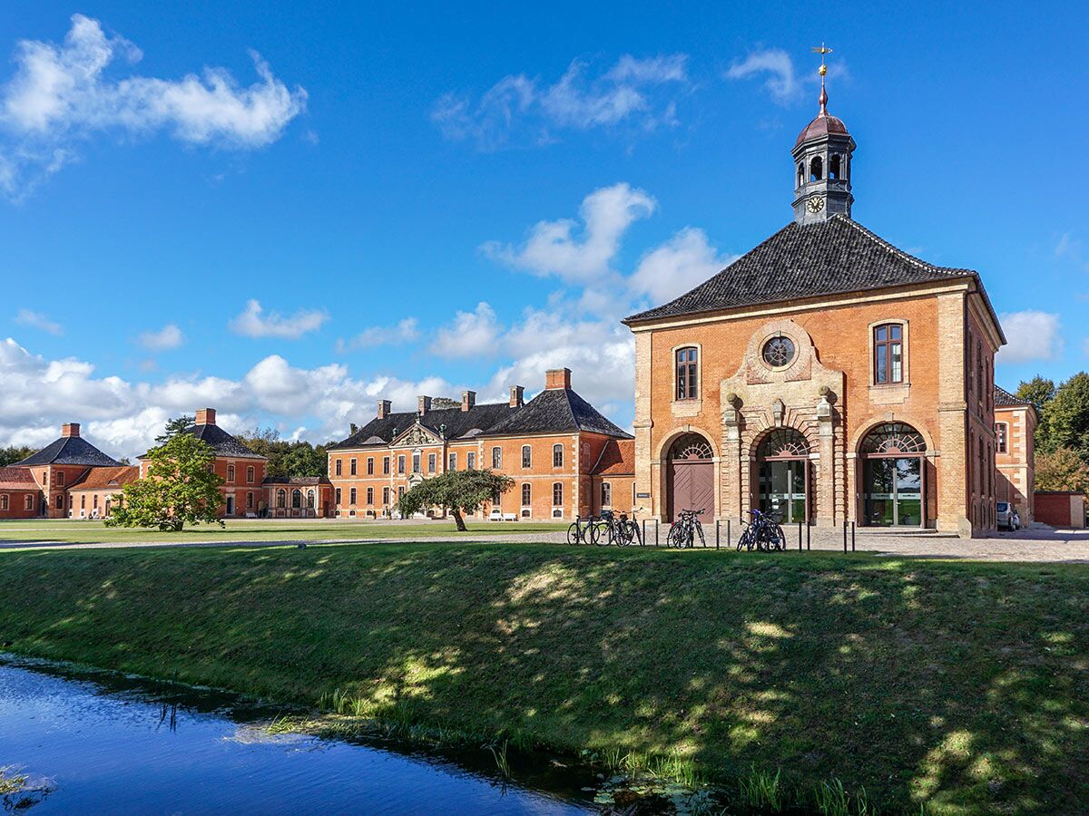 Historisches Schloss Augustenborg in Dänemark mit roten Backsteingebäuden, Grünflächen, Kanal und blauem Himmel.