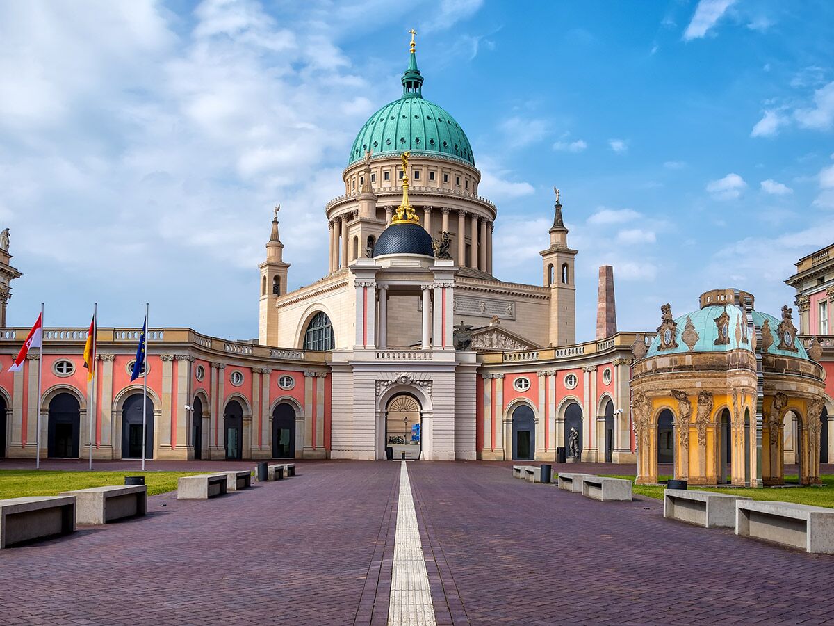 Potsdam Nikolaikirche Fassade, beeindruckende Architektur mit grüner Kuppel, Platz und Fahnen unter blauem Himmel.