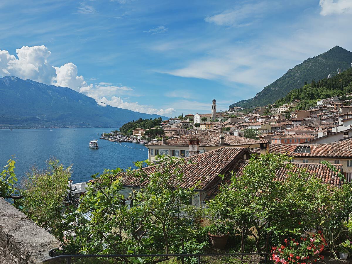 Malerische italienische Stadt am Gardasee mit terracotta Dächern, Kirchturm, Bergen und blauem See mit Fähre.