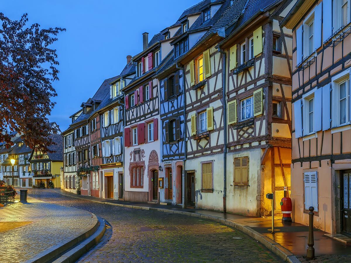 Nachtaufnahme einer romantischen Gasse in einer europäischen Altstadt mit beleuchteten Fachwerkhäusern und Kopfsteinpflaster bei Dämmerung.