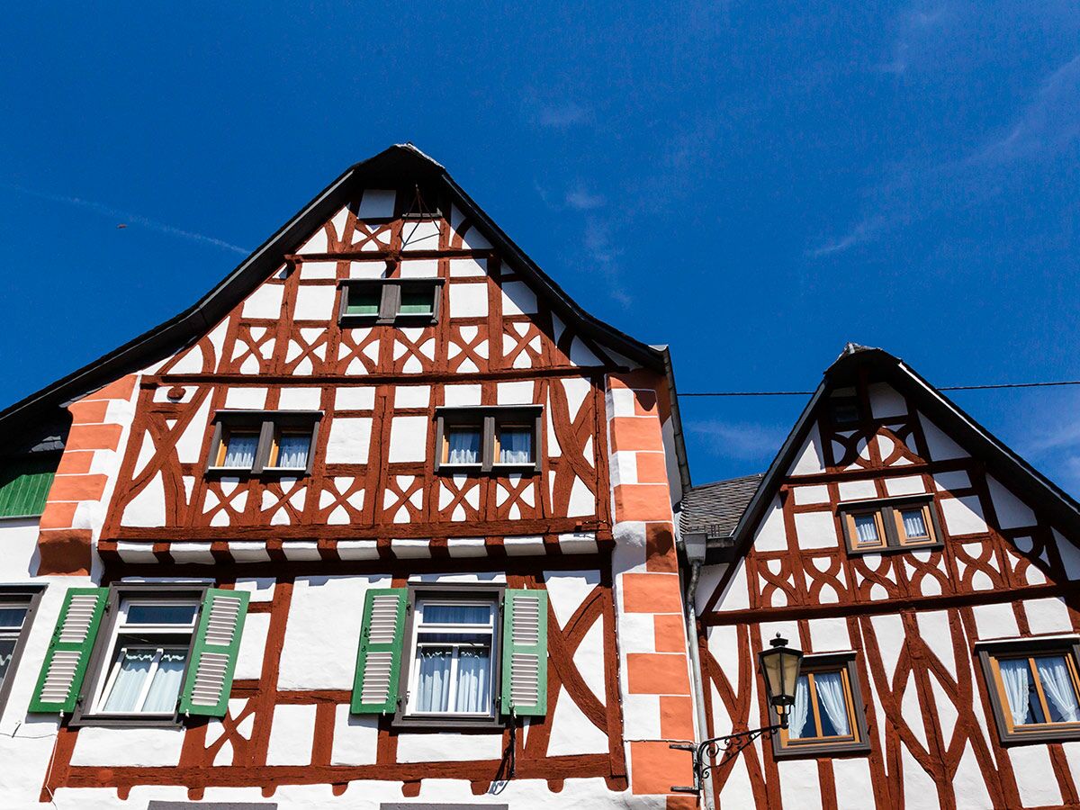 Fassaden traditioneller Fachwerkhäuser mit roten Holzbalken, weißen Wänden und grünen Fensterläden vor blauem Himmel.