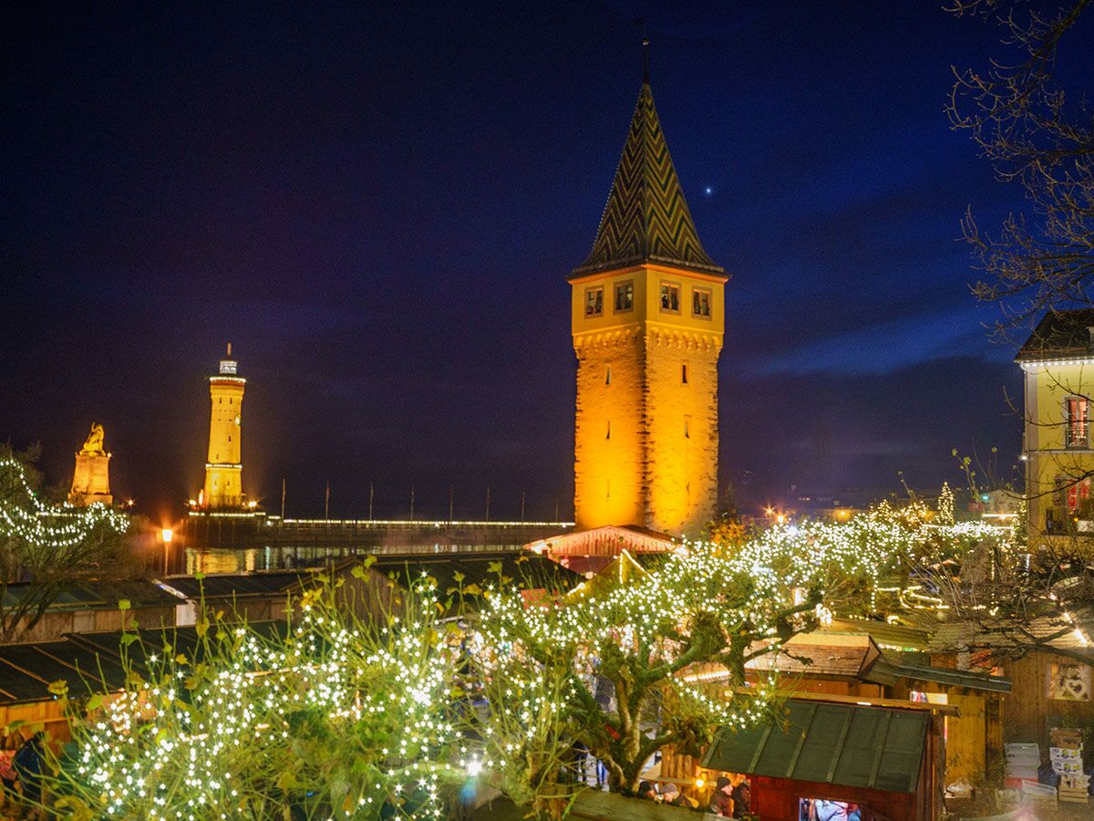 Beleuchteter Weihnachtsmarkt am Hafen Lindau bei Nacht mit Mangturm, Leuchtturm und Bodensee, festliche Atmosphäre.
