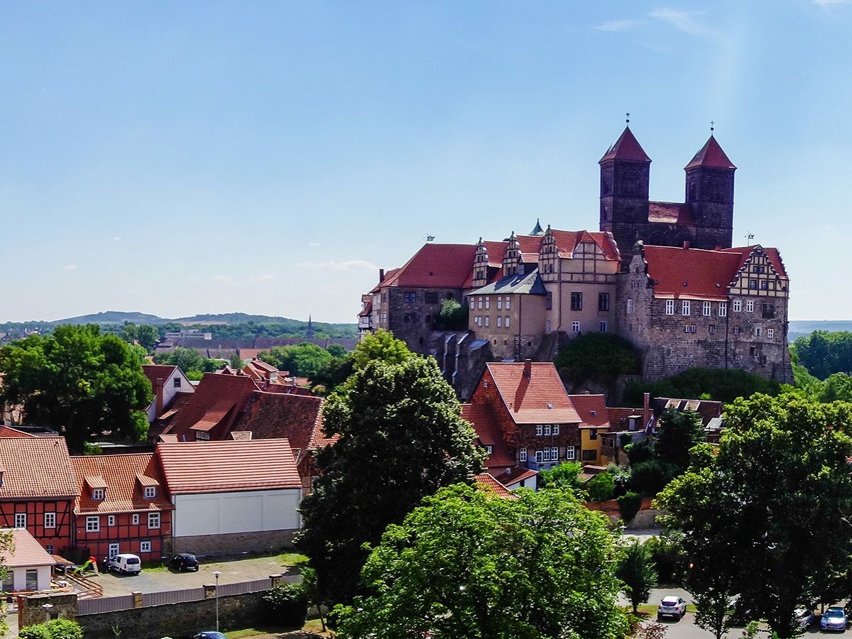 Panoramablick auf die historische Burg Quedlinburg und Fachwerkhäuser unter blauem Himmel.