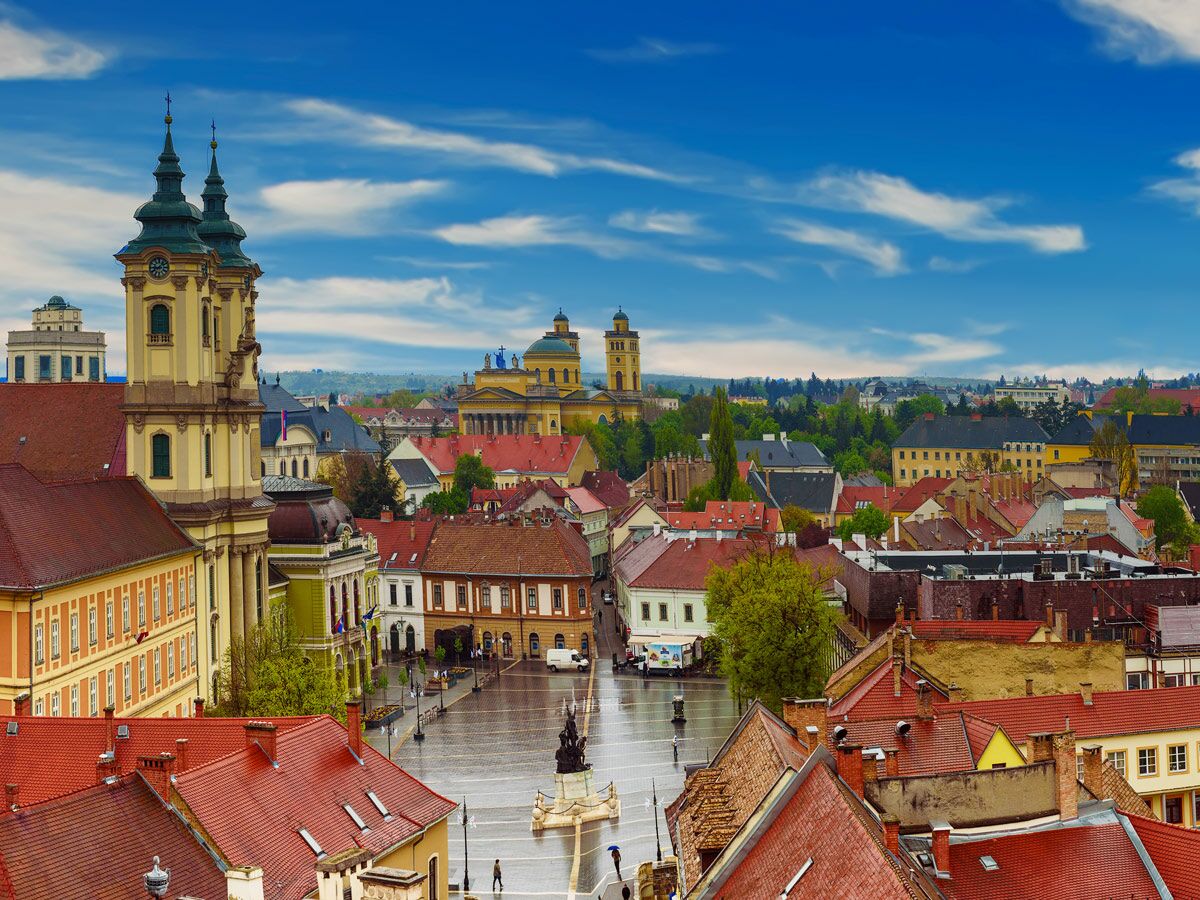 Panoramablick auf die historische Stadt Eger, Ungarn, mit der Minoritenkirche, roten Dächern und dem Hauptplatz bei blauem Himmel.